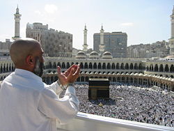 A supplicating pilgrim at Masjid Al Haram, the mosque which was built around the Ka`aba (the building at center). Thousands of pilgrims walk around the Kaaba in a counter-clockwise direction.
