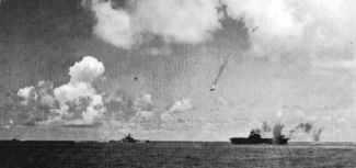A Japanese Val dive bomber (center) is shot down during the attack on the Enterprise (lower right). Enterprise is smoking from earlier bomb hits as another bomb near-misses the carrier. In the lower middle is the battleship USS South Dakota.