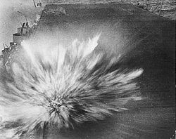 The third and last bomb, dropped by an aircraft piloted by Kazumi Horie who died in the attack, hits Enterprise, causing minor damage. Smoke from the first two bomb hits can be seen in the upper left of the picture.
